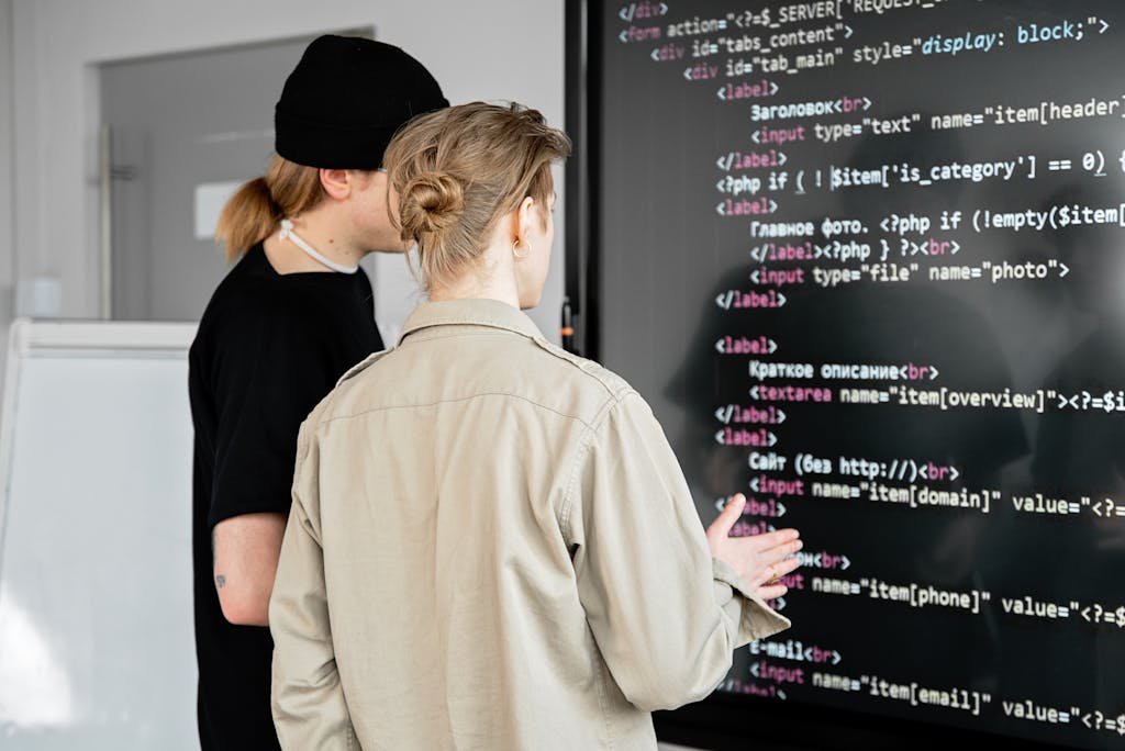 Two developers examining code on a large screen in a modern office space, focusing on web development.